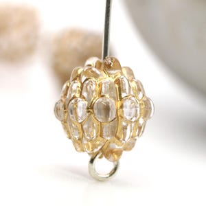 May include: A gold and clear glass bead with a faceted design. The bead has a small loop at the bottom for attaching to jewelry.