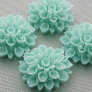 May include: Four aqua blue resin flower embellishments with a raised, detailed design. The flowers are arranged in a circle on a white background.