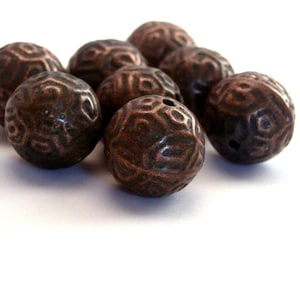May include: A group of ten copper-colored beads with a textured, geometric design. The beads are round and have a hole in the center.
