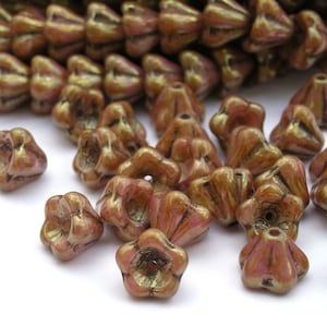 May include: A close-up of a pile of small, iridescent, flower-shaped glass beads. The beads are a mix of pink and brown with a metallic sheen.