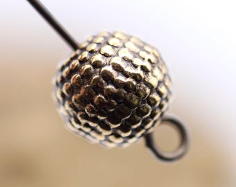 Könnte beinhalten: Eine goldfarbene Metallperle mit strukturierter Oberfläche. Die Perle hat eine kleine Schlaufe an der Seite.