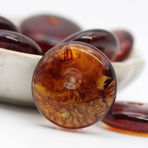 May include: A close-up of a round, amber-colored glass bead with a swirling pattern. The bead has a hole in the center for stringing.