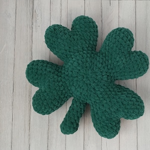 Könnte beinhalten: Ein dunkelgrünes, kleeblattförmiges Kissen. Das Kissen besteht aus einem weichen, strukturierten Material und hat die Form eines dreiblättrigen Kleeblatts. Dieser Artikel ist zum Thema St. Patrick's Day.