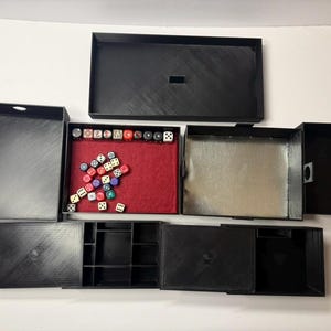 May include: A black, multi-compartment dice rolling and storage box. The box is open, revealing a red felt rolling surface, dice, and storage areas. The box is designed to hold and organize dice for tabletop games.