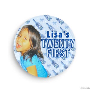 May include: A round button with a light blue background featuring a young person and the text "Lisa's TWENTY FIRST" in blue. The background has a pattern of blue bottles and bows.