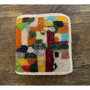 May include: A square beaded coaster or mat featuring a geometric mosaic pattern in shades of yellow, orange, red, green, blue, and purple. The piece is bordered by a single row of small, cream-colored beads along all four edges.