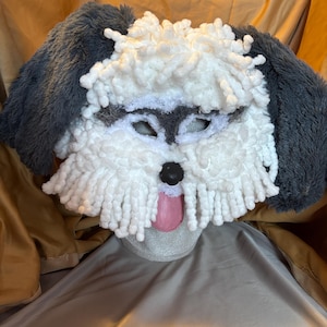 May include: A white and gray dog mask with a fluffy white face and gray ears. The mask has a pink tongue sticking out and black eyes.