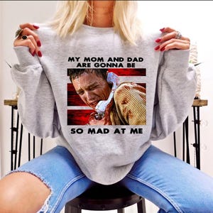 Puede incluir: Sudadera gris con un gráfico de una persona al teléfono con el texto "My mom and dad are gonna be so mad at me".