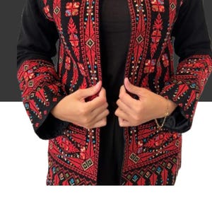 May include: Black jacket with detailed red embroidery. The jacket has floral and geometric patterns on the edges and sleeves. The text "Discover the art of Tareez with our unique and elegant pieces" is displayed.