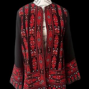 May include: Black jacket with detailed red embroidery. The open-front jacket showcases intricate patterns on the front, sleeves, and cuffs. The embroidery incorporates geometric and floral designs, providing a striking contrast against the black fabric. The jacket is displayed on a mannequin.