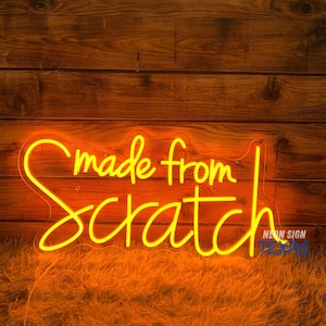 May include: A neon sign with the words "made from scratch" in a yellow, cursive font. The sign is against a wooden background and sits on a bed of orange shag carpet. The sign also has the words "NEON SIGN TEXAS" in blue.