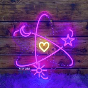 May include: A neon sign with a heart, star, moon, and sun design in pink and yellow. The sign is mounted on a wooden background and sits on a purple fluffy surface. The text "NEON SIGN TEXAS" is visible.