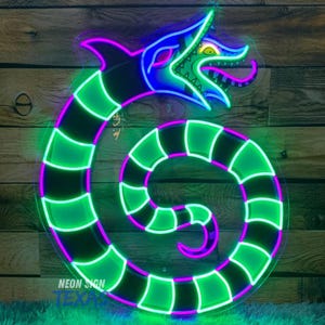 Puede incluir: Un letrero de neón con la forma de un dragón estilizado. El dragón es principalmente verde y negro, con acentos rosas y azules. El letrero tiene el texto "NEON SIGN TEXAS" en la parte inferior.