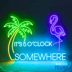Könnte beinhalten: Ein Neonschild mit einer grünen Palme auf der linken Seite und einem violetten Flamingo auf der rechten Seite. Der Text IT'S 5 O'CLOCK SOMEWHERE leuchtet hellblau in der Mitte. Das Schild ist auf einem transparenten Träger montiert.