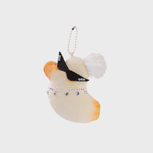 May include: A plush, cream-colored koala bear ornament with brown ears and a white pom-pom tail. It wears a black felt bow and a sparkling rhinestone necklace. A beaded chain is attached for hanging.