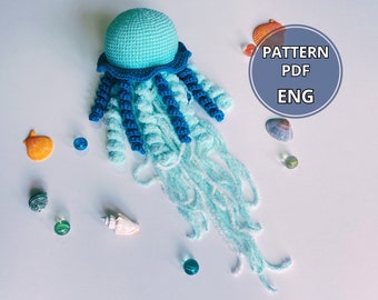 May include: Crochet pattern for a blue and turquoise jellyfish amigurumi toy. The pattern is in English and is available as a PDF download. The image shows the finished toy and some seashells.