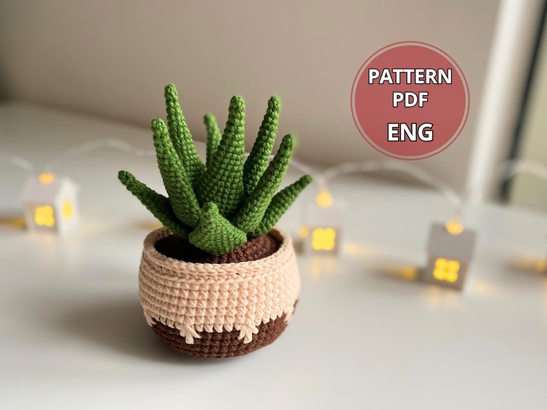May include: Crochet pattern for a green and brown succulent plant in a pot. The pattern is available in English and is in PDF format.