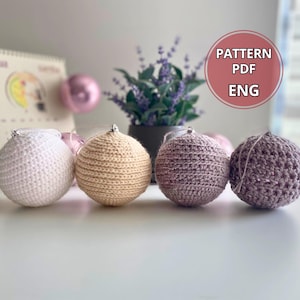 Puede incluir: Cinco adornos navideños de ganchillo en blanco, beige y morado. Los adornos están dispuestos en una fila sobre una superficie blanca. El texto "PATTERN PDF ENG" es visible en la esquina superior derecha de la imagen.