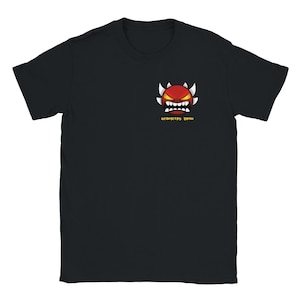 May include: Black t-shirt featuring a red, angry-faced cartoon character with white spikes and teeth. The text "GEOMETRY DASH" is printed in yellow below the graphic. The shirt is a short-sleeved crew neck.