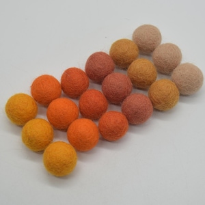 Könnte beinhalten: Eine Sammlung von 18 Filzkugeln in Orange-, Rot- und Beigetönen. Die Kugeln sind in einem Farbverlauf von Hellbeige bis Dunkelorange angeordnet.