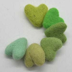 Op de afbeelding: Een set van zes vilt hartversieringen in tinten groen en lichtblauw. De harten zijn in een cirkel gerangschikt, met het grootste hart bovenaan en het kleinste hart onderaan.