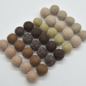 Peut inclure: Une collection de boules de feutre dans différentes nuances de brun, beige et vert. Les boules sont disposées en dégradé, les couleurs les plus claires en haut et les couleurs les plus foncées en bas.