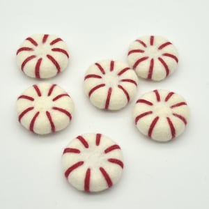 May include: Six felt peppermint candies with red and white stripes. The candies are arranged in a semi-circle on a white surface.