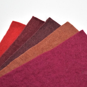 May include: Five different shades of felt fabric swatches, ranging from a deep burgundy to a light red. The swatches are arranged in a fan shape, with the darkest shade at the bottom and the lightest shade at the top.