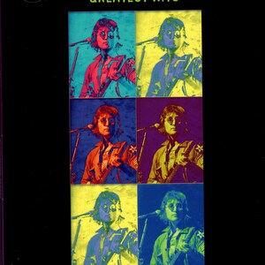 May include: A John Lennon "Greatest Hits" music score book. The cover features a grid of six color-shifted images of John Lennon playing a guitar and singing into a microphone. The title is in orange and white text on a black background.