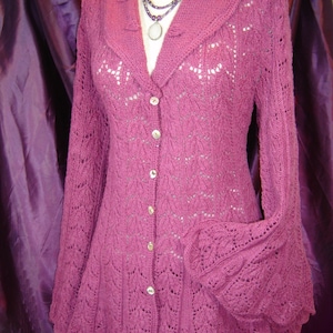 May include: A long-sleeved, mauve cardigan with a lace pattern and a button-up front. The cardigan has a wide collar and bell sleeves.