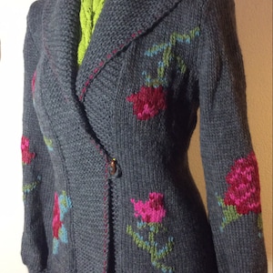 Può includere: Un blazer grigio lavorato a maglia con collo a scialle e ricami floreali. Il blazer presenta rose rosa e rosse con accenti verdi e blu. Chiusura con un solo bottone e cuciture rosse.