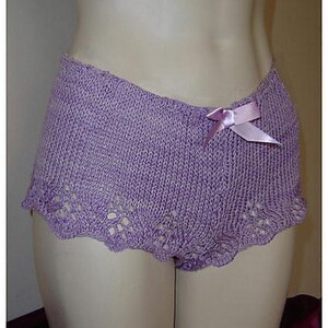 May include: Lilac knitted shorts with a scalloped edge and a small bow. The shorts are displayed on a mannequin. The knitwear has a delicate, openwork design along the bottom edge, adding a touch of elegance to the garment.