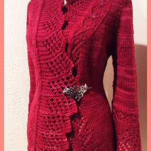 May include: A red knitted jacket with intricate openwork and a high collar. The jacket features a decorative silver brooch and long sleeves with openwork cuffs. The overall design is elegant and detailed, showcasing a blend of textures.