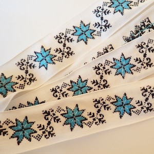 Pode incluir: Fita branca com um padrão repetido de estrelas azuis e pretas. A fita é tecida com um design geométrico simples.