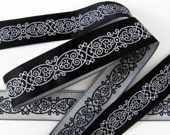 May include: Black and silver ribbon with a decorative, intricate pattern. The ribbon is woven with a repeating design of swirls and loops.