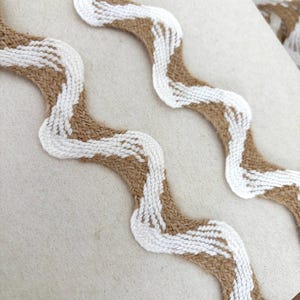 May include: White and brown wavy trim with a zig-zag pattern. The trim is made of a woven material and is perfect for adding a touch of texture to your projects.