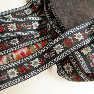 Black jacquard fabric ribbon trim with white edelweiss flowers and blue and red alpine flowers and touches of brown, black and white edges