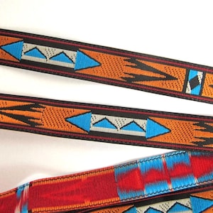 May include: A woven fabric strap featuring a repeating geometric pattern in orange, black, white, and bright blue. The design includes pointed arrow-like shapes and triangular motifs. A section of the strap displays a vibrant red and blue gradient.