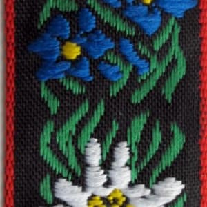 jacquard trim with white edelweiss flowers, blue flowers, green leaves and four red hearts, on black with red woven edges, bavarian trim