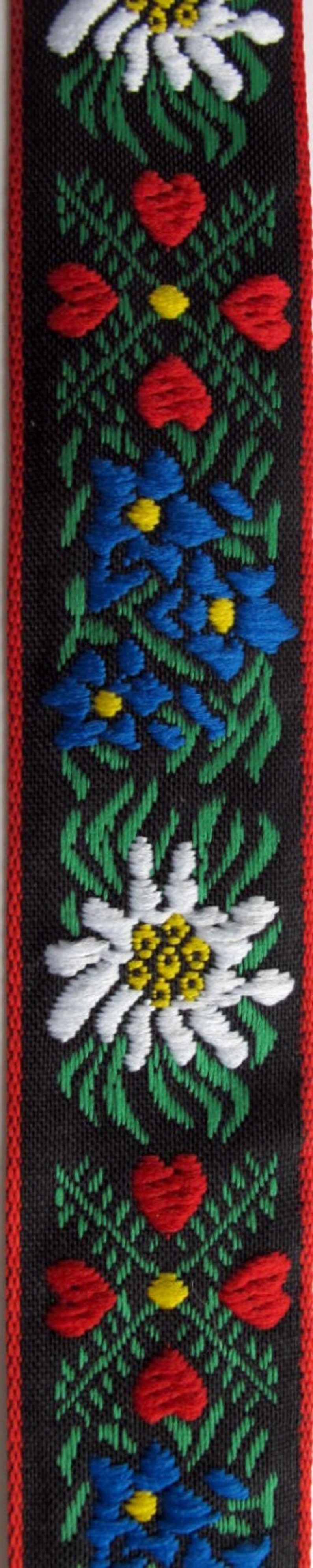 jacquard trim with white edelweiss flowers, blue flowers, green leaves and four red hearts, on black with red woven edges, bavarian trim