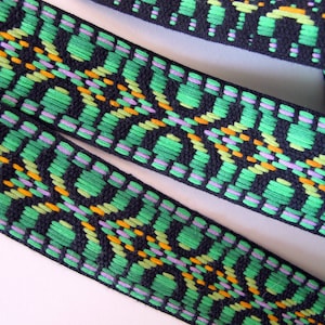 May include: Close-up of black, green, orange, and purple woven ribbon with a geometric pattern.