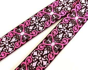 May include: Pink and brown patterned ribbon with a repeating geometric design. The ribbon is woven with a white thread.