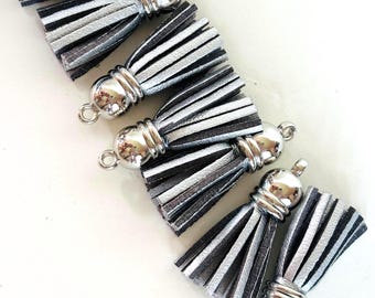 May include: Six silver and black tassels with a metallic finish. Each tassel has a silver cap and a small loop for attaching to a keychain or other craft project. The tassels are arranged on a white surface.