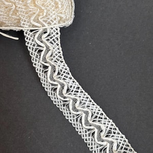 Könnte beinhalten: Elfenbeinfarbenes Zierband mit gewebtem, offenem Design. Das Band hat ein Zickzackmuster an den Kanten, das einen strukturierten und eleganten Touch verleiht. Das Band befindet sich auf einer Rolle und ist für verschiedene Bastelprojekte geeignet.
