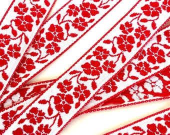 May include: Red and white woven ribbon with a floral pattern. The ribbon is approximately 1 inch wide.