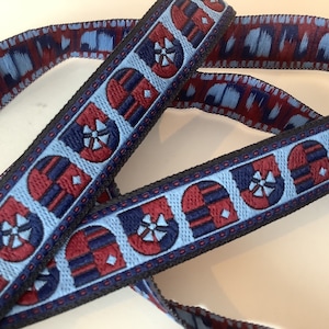 Könnte beinhalten: Nahaufnahme eines dekorativen Bandes mit sich wiederholendem Muster. Das Band hat einen hellblauen Hintergrund mit einem geometrischen Design in Marineblau und Rot. Die Ränder sind mit einem schwarzen Besatz versehen.