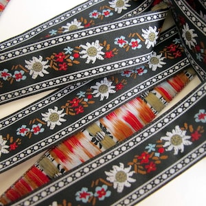 Black jacquard fabric ribbon trim with white edelweiss flowers and blue and red alpine flowers and touches of brown, black and white edges
