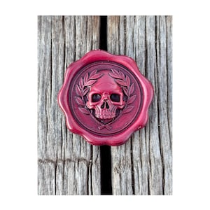 Könnte beinhalten: Ein burgunderfarbenes Wachssiegel mit einem Totenkopf- und Lorbeerkranz-Design. Der Totenkopf befindet sich in einem kreisförmigen Rahmen, umgeben von einem Kranz. Zwei gekreuzte Schwerter befinden sich darunter. Das Siegel liegt auf einer verwitterten Holzoberfläche.