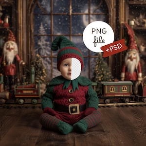 May include: A baby dressed in a red and green elf costume sits on a wooden floor in front of a Christmas scene. The costume includes a hat, tunic, and striped socks. The background features a snowy window, toy trains, and Christmas decorations. The image includes the text "PNG file + PSD".