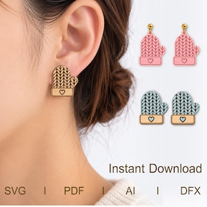 May include: A pair of mitten-shaped earrings featuring a knit texture pattern and a small heart detail at the cuff. The design is shown in natural wood, pink, and light blue. The image includes the text BS Digital craft and Instant Download SVG PDF AI DFX.
